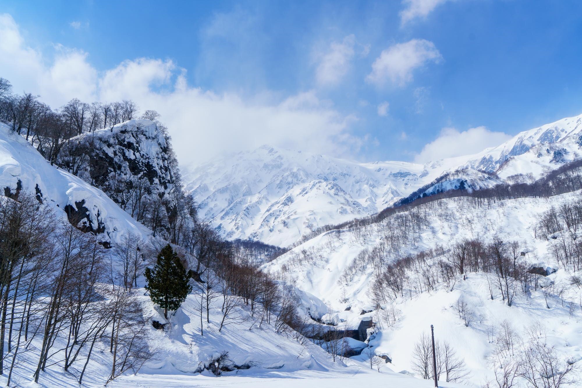 青空と雲の下に広がる、雪に覆われた山並み