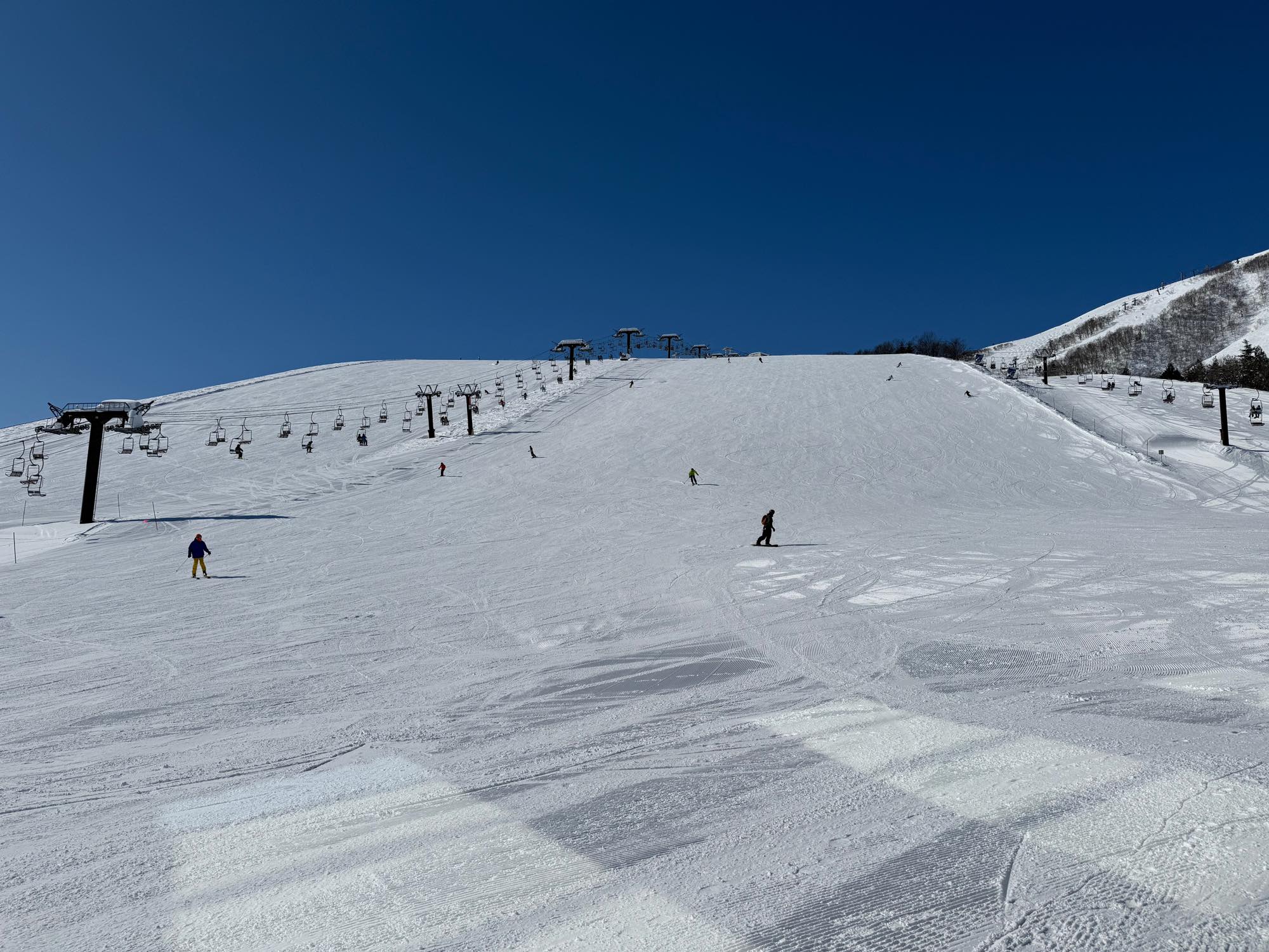 青空の下、スキーヤーが滑る広い雪のゲレンデとリフト