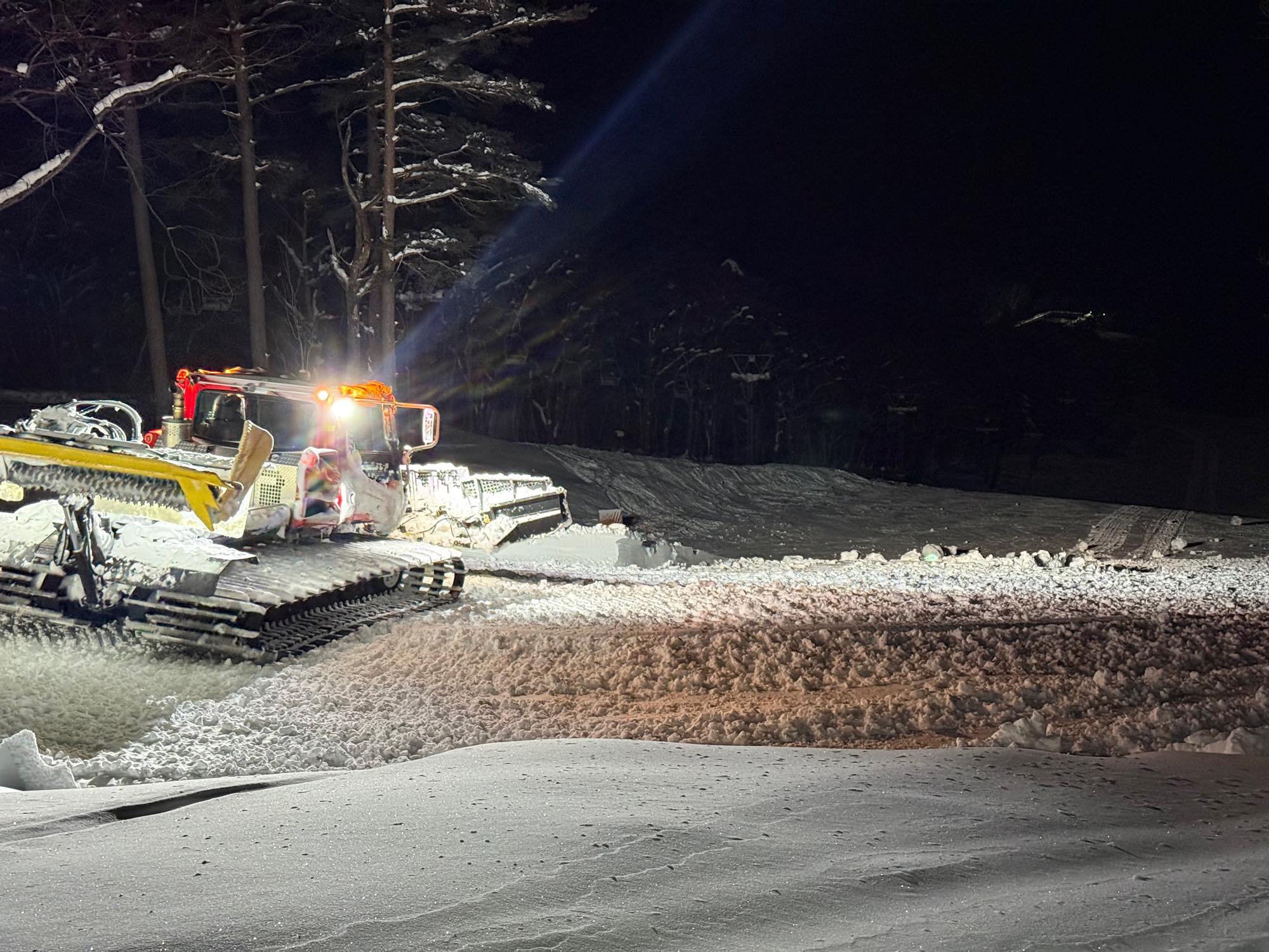 圧雪車が雪の山を押し広げて滑走面をつくる様子