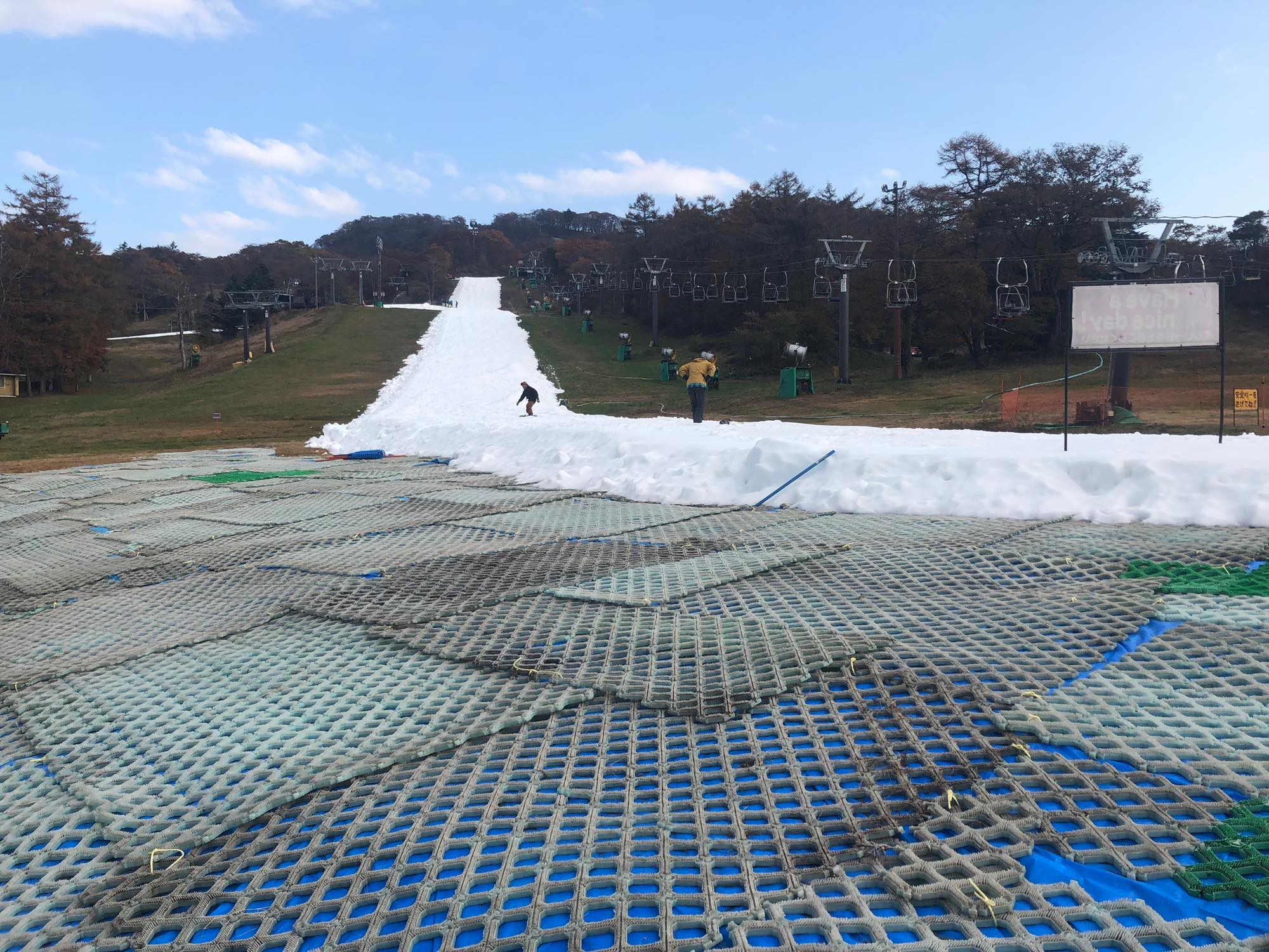 周囲に草地が残るなか、白いコースでスノーボードを楽しむ初滑り期の風景